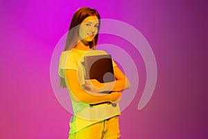 Portrait of young girl, student posing with tablet isolated over pink background in neon light. New education year