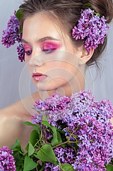 Portrait of a young girl in the studio with lilac flowers on her head, close-up. Creative beautiful make-up in doll