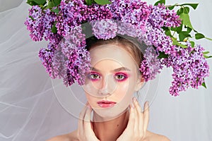 Portrait of a young girl in the studio with lilac flowers on her head, close-up. Creative beautiful make-up in doll