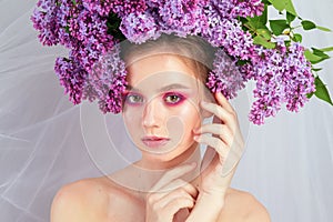 Portrait of a young girl in the studio with lilac flowers on her head, close-up. Creative beautiful make-up in doll