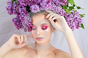 Portrait of a young girl in the studio with lilac flowers on her head, close-up. Creative beautiful make-up in doll