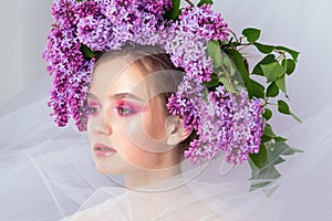 Portrait of a young girl in the studio with lilac flowers on her head, close-up. Creative beautiful make-up in doll