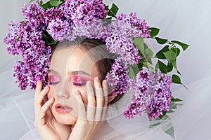 Portrait of a young girl in the studio with lilac flowers on her head, close-up. Creative beautiful make-up in doll