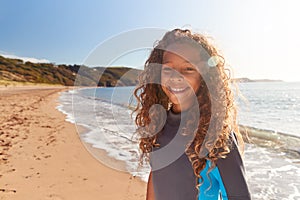 Portrait Of Young Girl Wearing Wetsuit Standing By Waves On Summer Beach Vacation