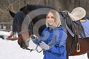 Portrait of a young girl with white hair next to a brown horse. The girl holds the horse and smiles. Close-up