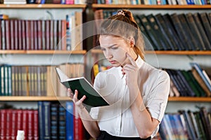 Portrait of a young girl who is reading a book in the library.