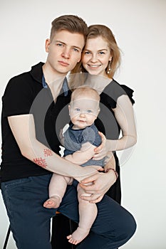 Portrait of young good-looking family in dark clothes with plump cherubic baby infant sitting on white background.