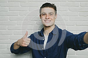 Portrait of young goodlooking man with thumbs up against white brickwall.