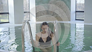 Portrait of young gorgeous brunette woman getting out of swimming pool and leaving. Smiling Caucasian lady in black