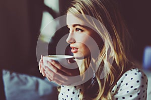 Portrait of young gorgeous female drinking tea and thoughtfully looking out of the coffee shop window while enjoying her leisure t