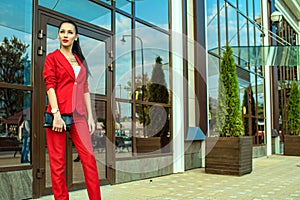 Portrait of young gorgeous lady with high pony tail in red costume and high-heeled shoes standing in front of mirrored shop window