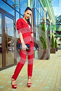 Portrait of young gorgeous lady with high pony tail in red costume and high-heeled shoes standing in front of mirrored shop window