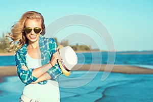 Portrait of young gorgeous suntanned blond wearing mirrored heart shaped sunglasses and checked blue shirt at the seaside