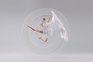 Portrait of young graceful ballerina dancing with transparent fabric isolated over grey studio background. Weightless