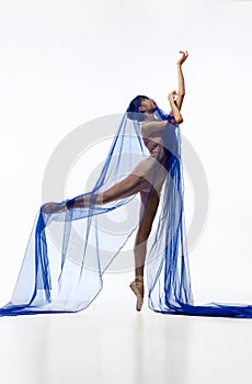 Portrait of young graceful Japanese ballerina dancing with transparent fabric, blue cobweb  on white studio