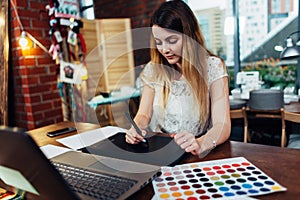 Portrait of young graphic designer working on new project using graphics tablet and laptop sitting in modern office