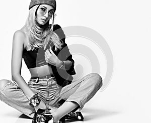 Portrait of young grunge style girl in torn jeans, bralet, boots and winter hat sitting cross-legged on floor