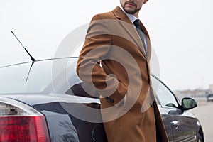 Portrait of a young guy, a businessman in a stylish business suit, with a thump, stands by the car. Business concept.