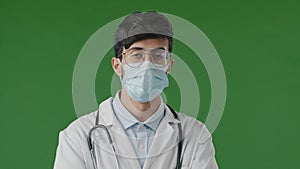 Portrait of young guy doctor in studio on green background serious hispanic man in protective medical mask and glasses