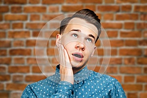 Portrait young guy dressed blue shirt. man open his eyes wide with hands, fingers and mouth. Man on brick wall background