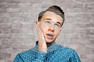 Portrait young guy dressed blue shirt. man open his eyes wide with hands, fingers and mouth. Man on brick wall background