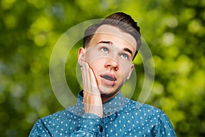 Portrait young guy dressed blue shirt. man open his eyes wide with hands, fingers and mouth. Man on green bokeh background