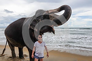 Portrait of a young guy with an elephant on the background of a tropical ocean beach. Elephant with trunk up
