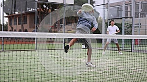 Portrait of young guy enjoying paddle tennis doubles game with adult male teammate on court outdoor