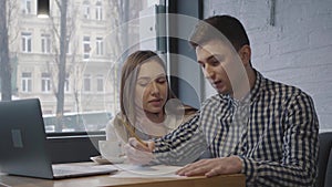 Portrait of a young guy and girl sitting at a table with a laptop near the window in a cozy cafe or restaurant. Friends