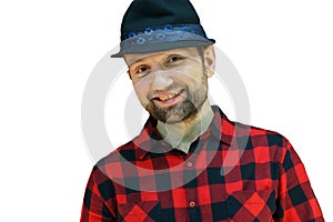 Portrait of a young guy in a hat and a red plaid shirt on a white background. A bearded man with a smile on his face