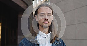 Portrait of young guy with long hair and earrings looking to camera.Close up view of millennial bearded hipster man