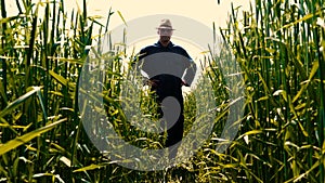 Portrait of a young guy man in a working uniform and a straw hat in the middle of a field around wheat and hay, running around i