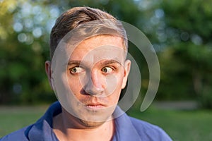 Portrait of a young guy on nature background. Puzzled confused bewildered shocked amazed man. comical reaction, emotion