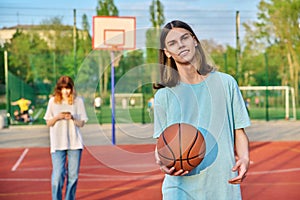 Portrait of young guy playing basketball on an outdoor game court, girl is out of focus.