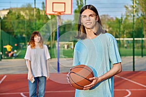 Portrait of young guy playing basketball on an outdoor game court, girl is out of focus.