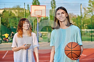 Portrait of young guy playing basketball on an outdoor game court, girl is out of focus.