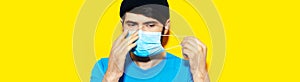 Portrait of young guy putting on a medical flu mask on face, protection against coronavirus or covid-19. Wearing blue shirt.