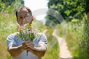Portrait of a young guy in a white T-shirt and with a bouquet of flowers in his hands. A guy poses against the background of a
