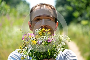 Portrait of a young guy in a white T-shirt and with a bouquet of flowers in his hands. A guy poses against the background of a