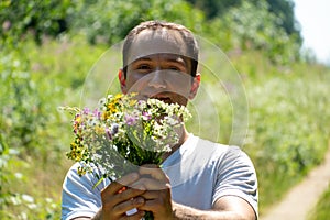 Portrait of a young guy in a white T-shirt and with a bouquet of flowers in his hands. A guy poses against the background of a