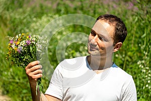 Portrait of a young guy in a white T-shirt and with a bouquet of flowers in his hands. A guy poses against the background of a