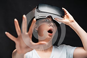 Portrait of young had shocked screaming woman removing VR glasses and reches hand. Black background. The concept of