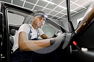 Portrait of young handsome African man worker in uniform and protective gloves performing the cleaning of car door with