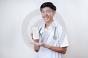 Portrait of young handsome Asian doctor showing phone with blank screen and copy space for medical app ads