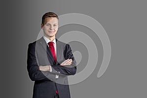 Portrait of young handsome, attractive blond man in suit and red tie on grey background