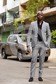 Full body shot of young handsome bald African businessman in suit outdoors