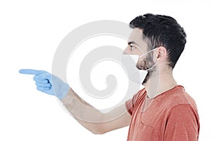 Portrait of young handsome beautiful man with face mask and blue gloves pointing side on copy space. 2019-nCoV.