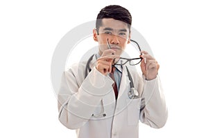 Portrait of young handsome brunette man doctor in white uniform take off his glasses and posing on camera isolated on