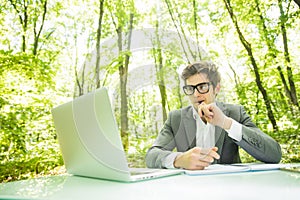 Portrait of young handsome business man in suit working at laptop at office table in green forest park. Business concept.