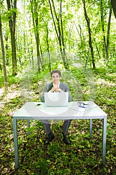 Portrait of young handsome business man in suit working at laptop at office table in green forest park. Business concept.